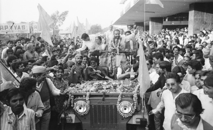 Crowds flock to a Jeep carrying a man and a woman