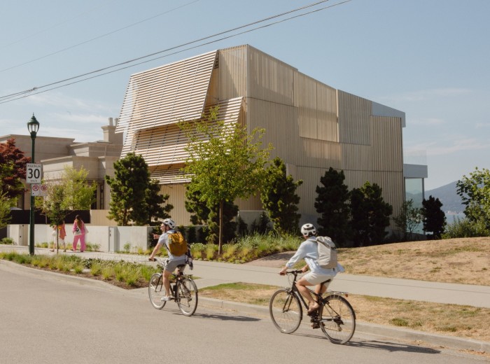 Cyclists passing by a property covered in slatted wooden panels on Vancouver’s Point Grey Road 