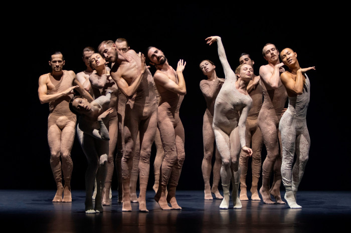 A group of male and female dancers in tight flesh-coloured costumes adopt various poses