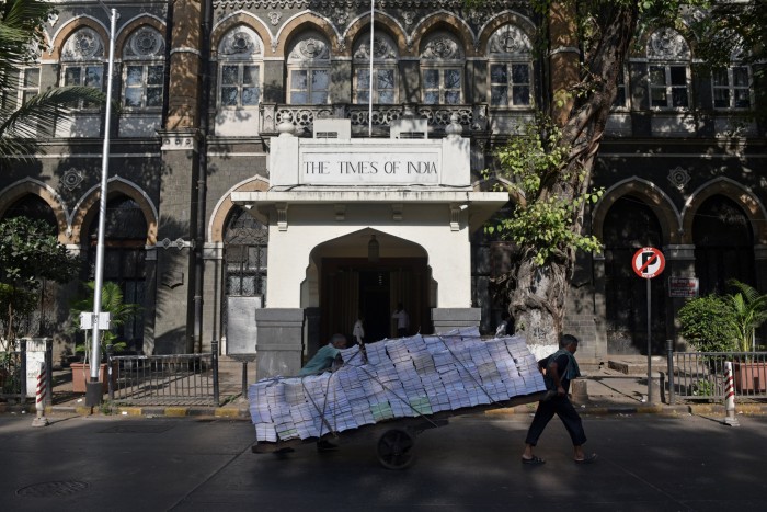 Day labourers pull a cart past the Times Of India headquarters building