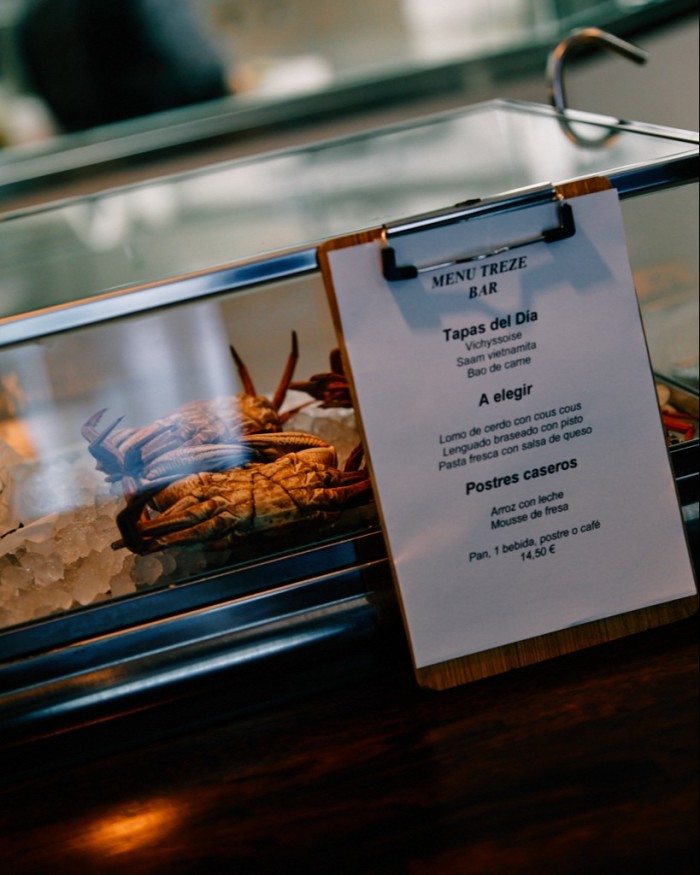 The menú del día at Treze printed on a piece of paper attached to a glass cabinet inside which are crabs on a bed of ice