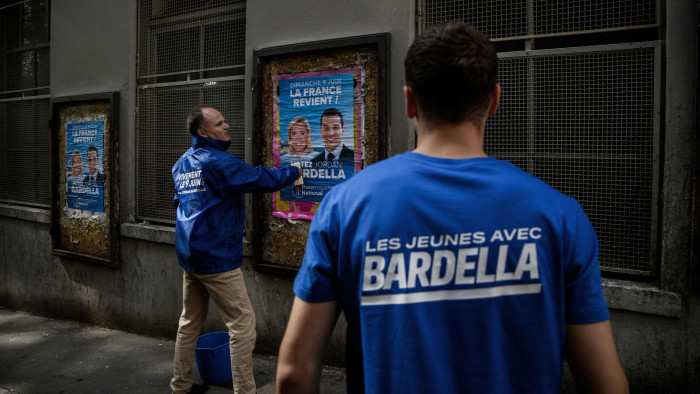 Two men paste French political posters on buildings