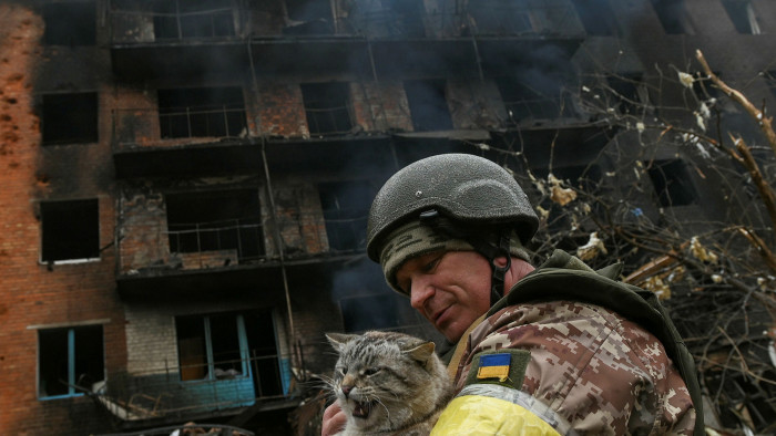 A Ukrainian service member holds a stray cat in front of a heavily damaged apartment building in the town of Valsylkiv, Ukraine