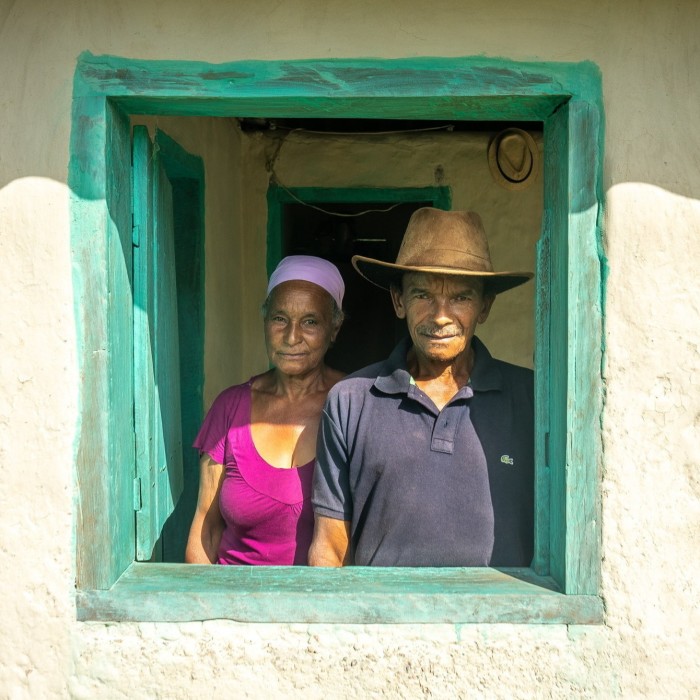 A couple stand in the bright-green frame of a window of their home