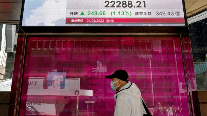 A man walks past an electronic board showing the Hong Kong share index 