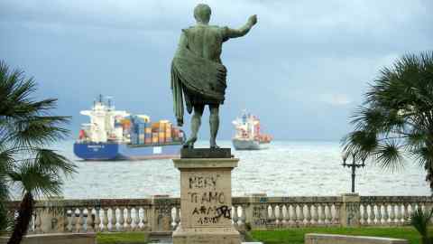 A statue of Julius Caesar in Naples looks out to sea towards a couple of container ships