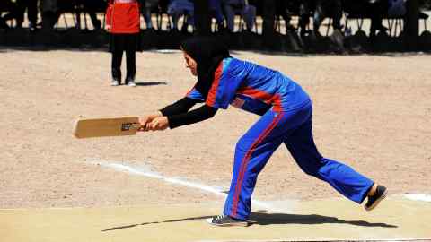 An Afghan wearing a blue tracksuit and hijab holds a cricket bat