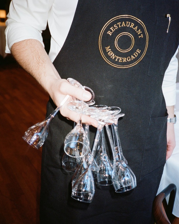 A male member of Møntergade’s waiting staff carrying wine glasses upside down by the stems 