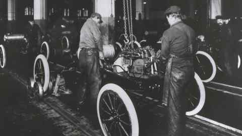 Workers construct a Model-T engine on an assembly line in a Ford Motor Company factory