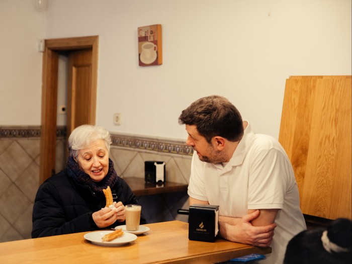  Churrería Apodaca’s Julio Cortijo at a table with one of his customers, who is holding a churro