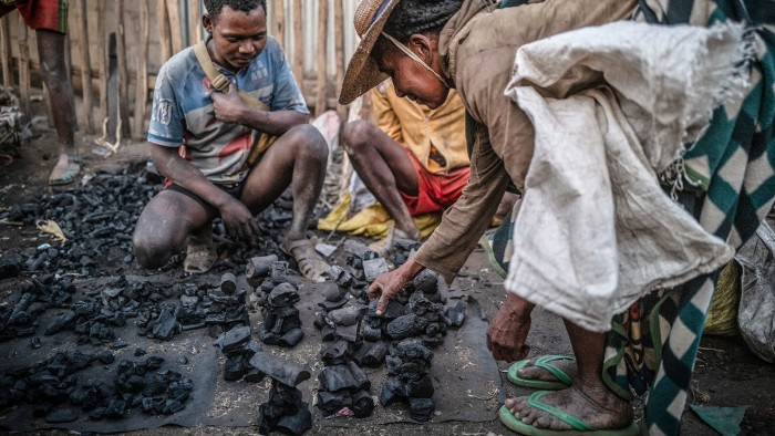 Three people looking at charcoal for sale at a market in Ambovombe, Madagascar