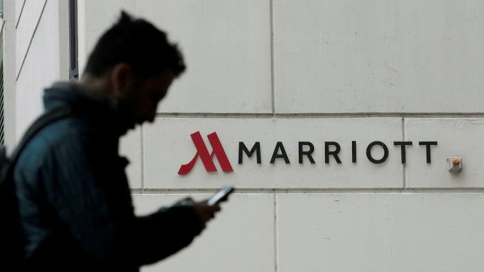 Man looking at his mobile phone and walking by a sign of a Marriott hotel