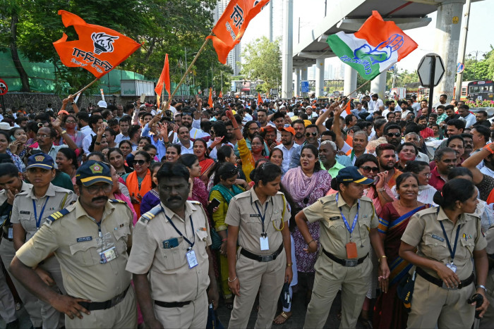 A crowd waves flags behind a line of police