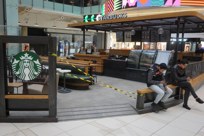 People seat on the bench in front of a Starbucks that is closed down