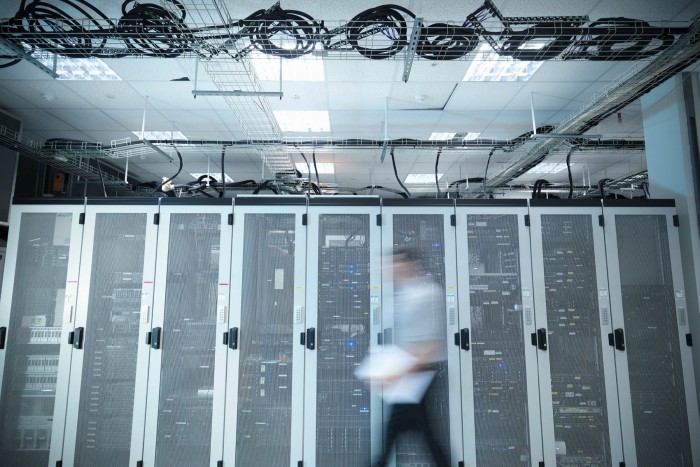 A blurred image of a man walking through a computer server room