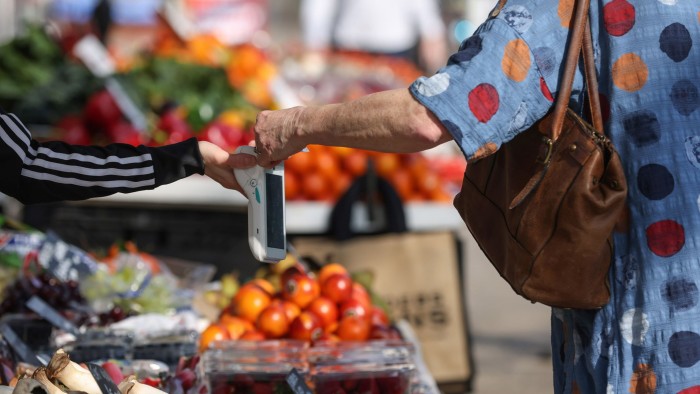 A shopper uses a card to touch a contactless payment terminal at  a fruit and vegetable stall at a market in Norwich, UK