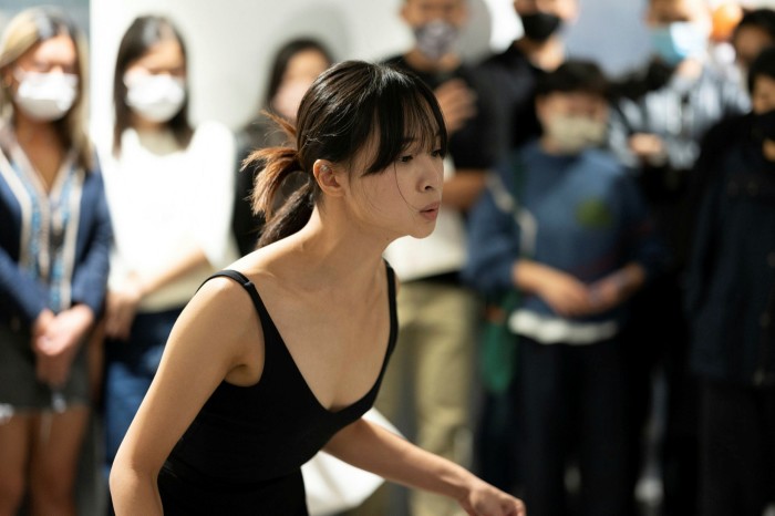 A woman in a black vest top giving a performance to a small crowd of people wearing face masks