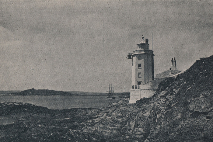 A black and white photo of a lighthouse on exposed rocks 