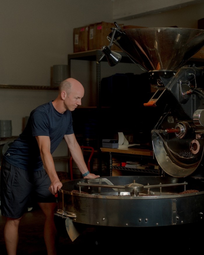 Elysian founder Alistair Durie leaning over a metallic coffee roasting machine