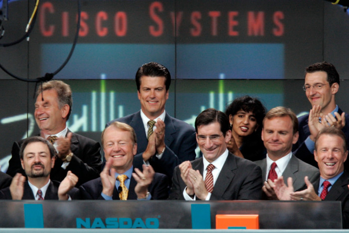 A group of executives stand in the trading hall of the Nasdaq exchange under a Cisco sign