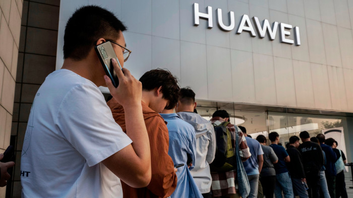 A man talks on a Huawei mobile phone as he and others line up to buy or reserve a new Mate 60 smartphone and other products outside a Huawei flagship store