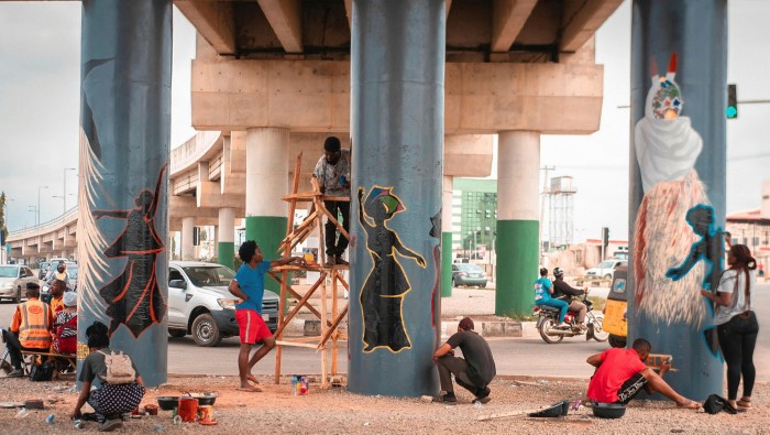 People painting concrete pillars under an elevated freeway