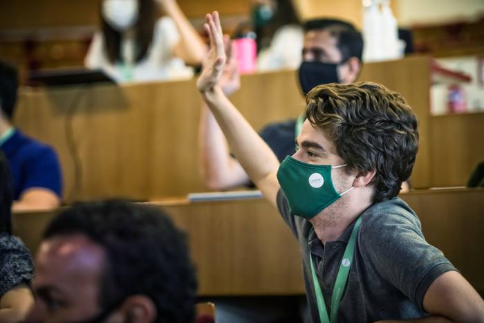 A male student with a face mask, raising his hand in class