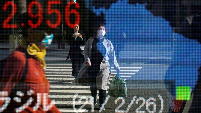 Passersby are reflected in a stock market indicator board in Tokyo