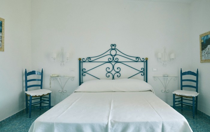 A bedroom at Hotel Punta Rossa, with white bedsheets and blue chairs either side