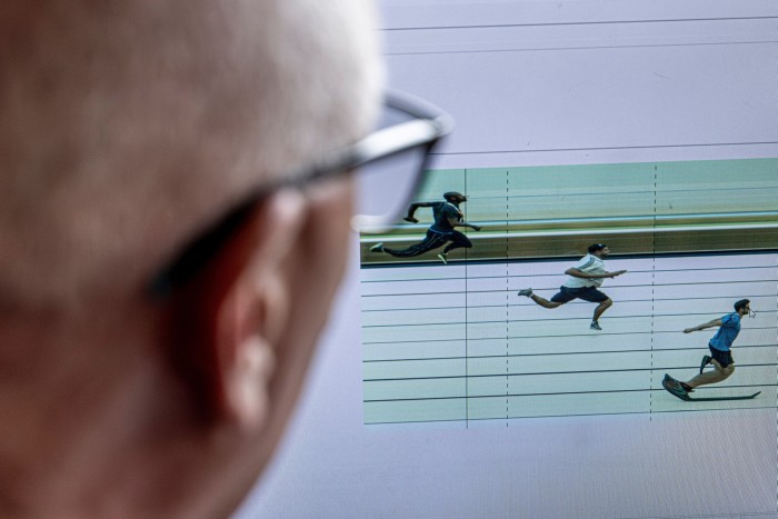 A man looks on to a video which shows three runners approach the finishing line at different times