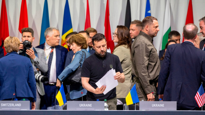 Ukraine’s President Volodymyr Zelensky, centre, looks at papers on a table with attendees in the background at the plenary session of the Summit on Peace in Ukraine the Burgenstock resort in Switzerland on Sunday