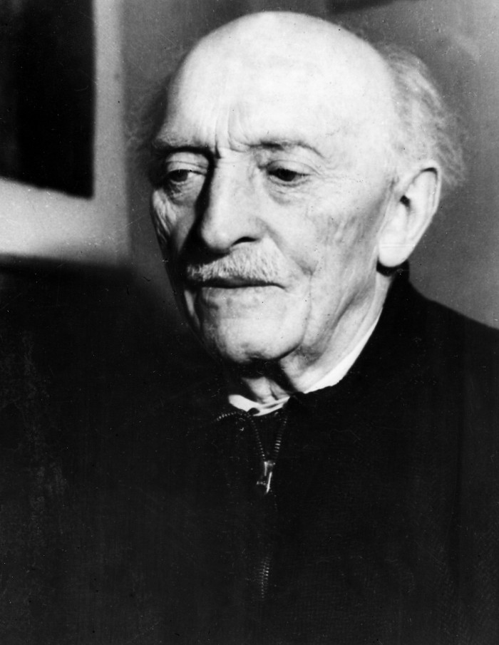 A black-and-white portrait of an old man with a grey moustache and a dark jumper