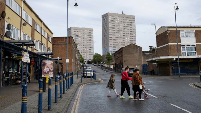 A family walks past a shopping area near social housing blocks in Birmingham