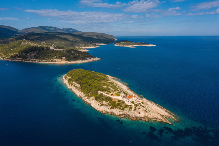 An aerial view of building at the end of an island in blue sea, with a coastline behind it