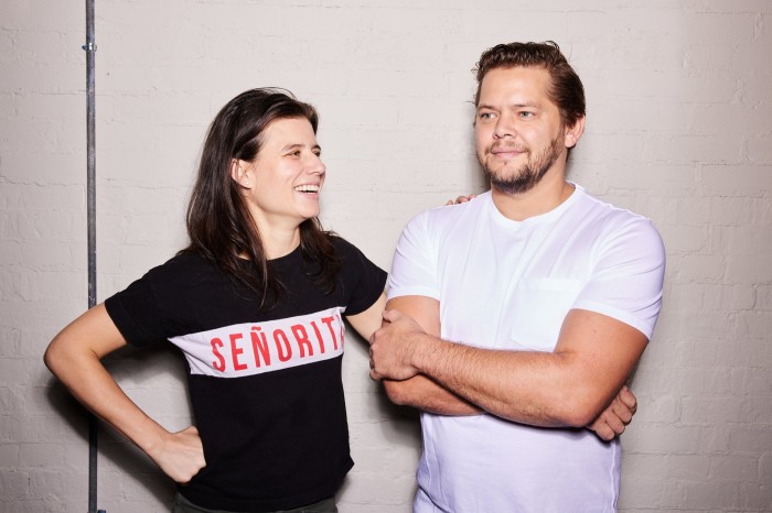 Luciana Giangrandi and Alex Meyer of Boia De: a woman in a black T-shirt that says ‘Señorita’ and a bearded man in a white T-shirt standing smiling