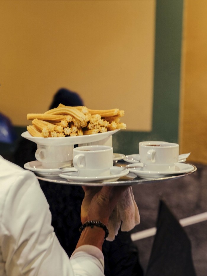 A waiter carrying a tray of cups and churros at the Chocolatería San Ginés 