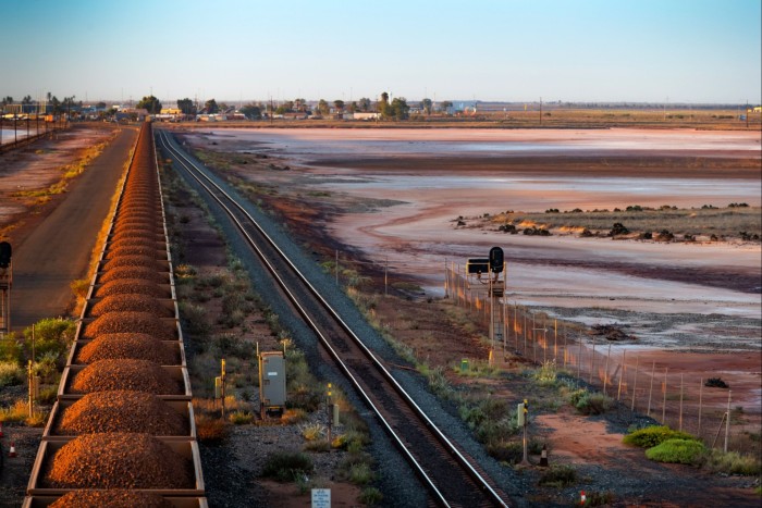 A freight train carrying iron ore travels along a rail track towards Port Hedland, Australia
