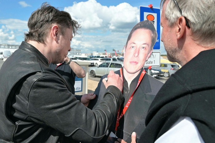 Elon Musk, left, signs a cardboard cut-out of himself during a visit to a Tesla factory under construction in Germany