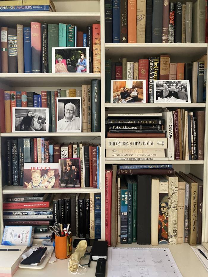 A desk in front of a bookcase, with family photographs on the shelves
