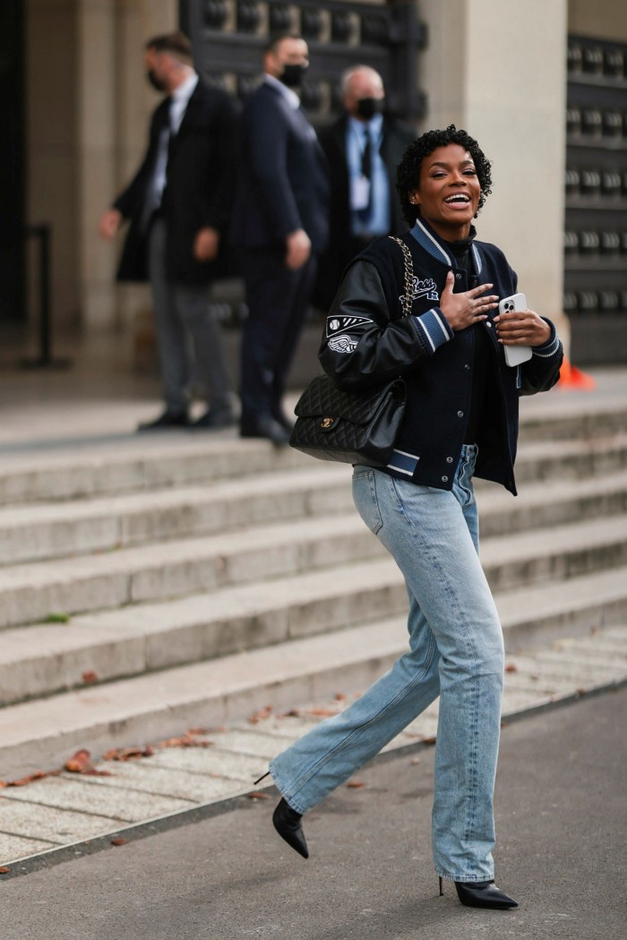 Didi Stone pairs a college jacket with blue jeans and heels outside L’Oréal