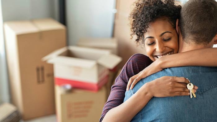 A couple embrace, surrounded by cardboard boxes, after moving to a new apartment