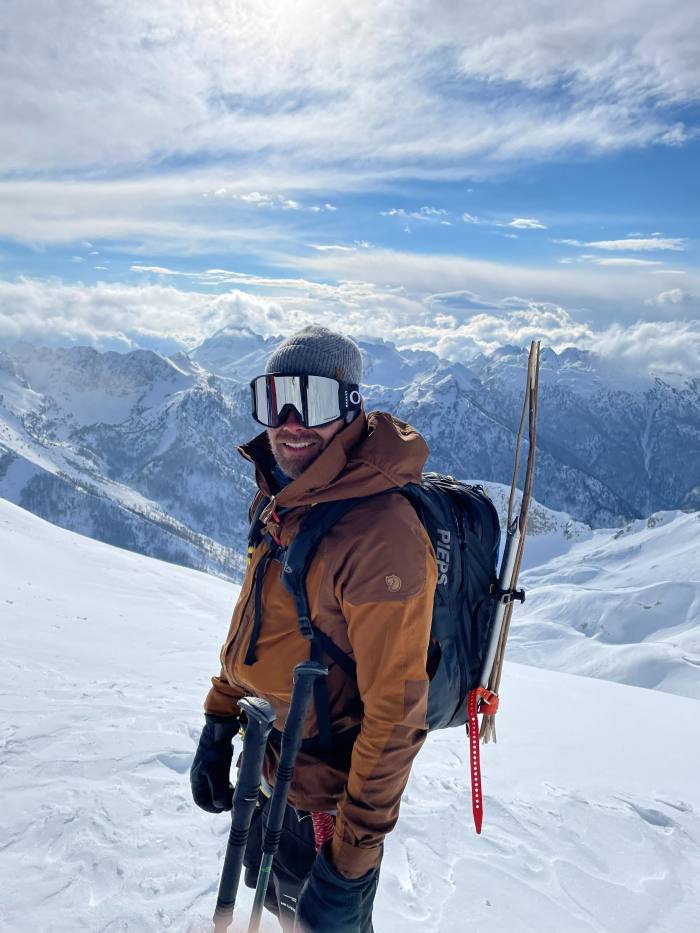 Ski instructor smiling at camera on top of snowy mountain in sunshine