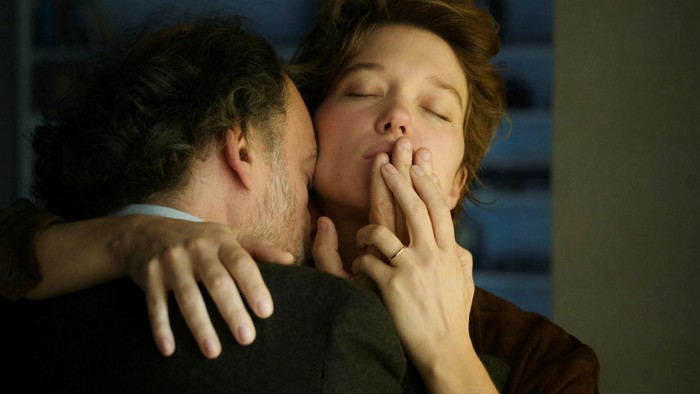 A man and a woman embrace with their eyes closed; she presses his fingers to her mouth