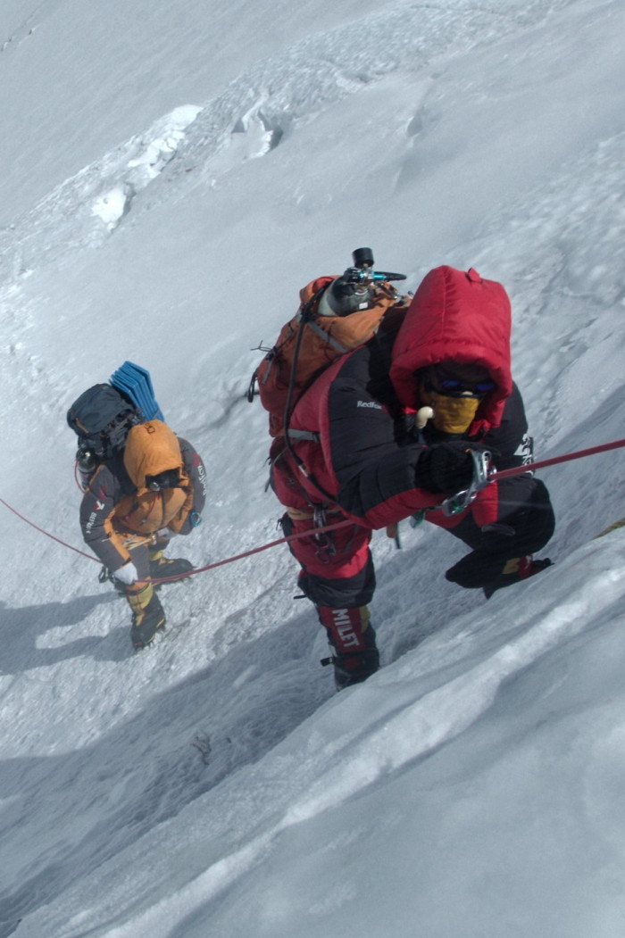 Two mountaineers in heavy winter layers make climb a steep icy ascent with ropes