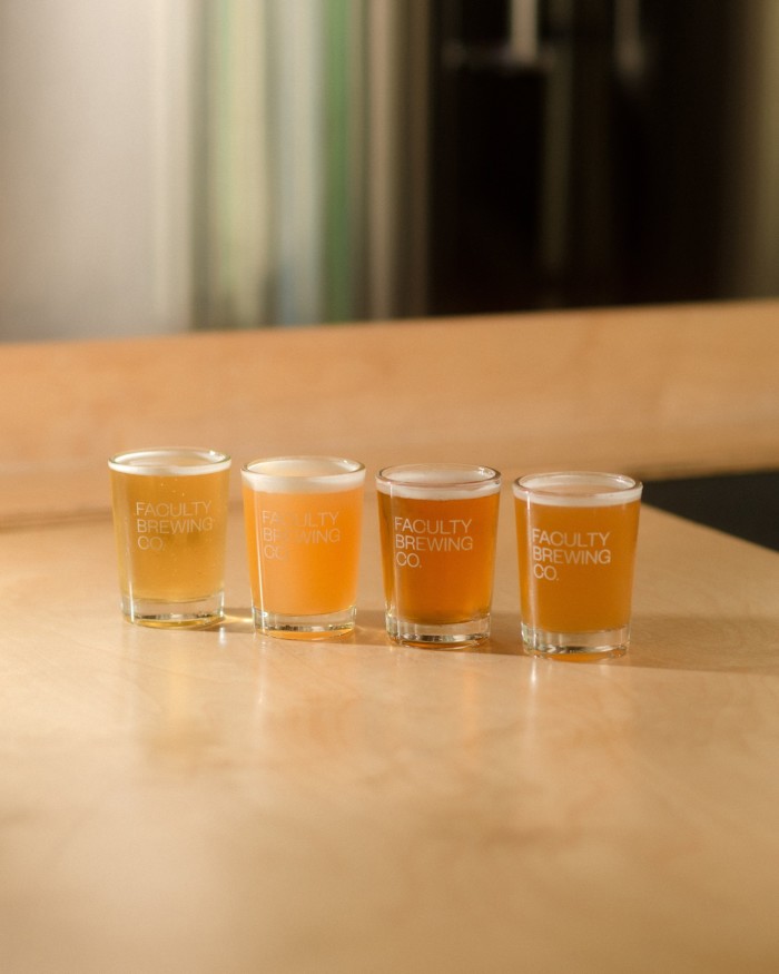 A flight of four glasses of beer on a blond-wood counter at Faculty