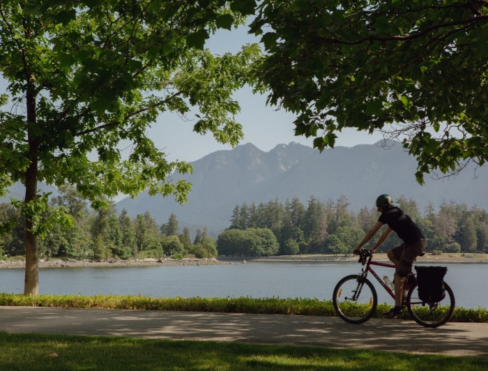A view of the mountains to the north of Vancouver harbour, as seen from Coal Harbour Park. A male cyclist is passing by on the path in the foreground