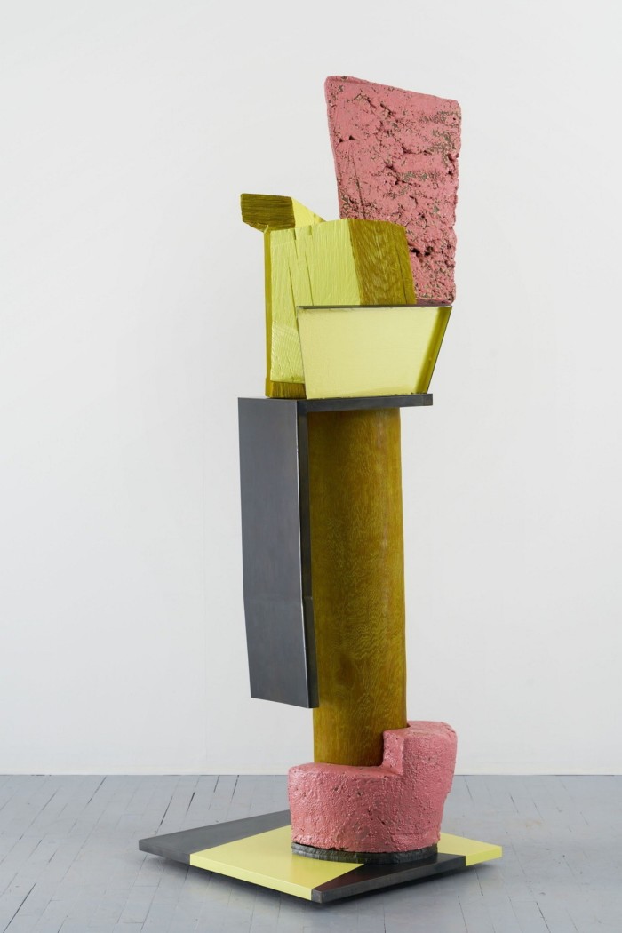 Tall sculpture with yellow and pink elements on a wooden stump 