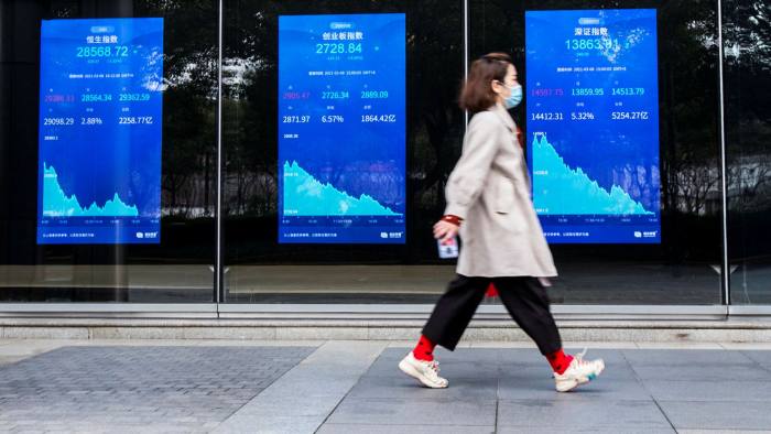 A woman walks past electronic screens showing stock prices