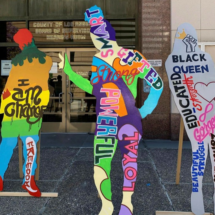 Three flat human-size and human-shaped figures brightly painted in rainbow colours 