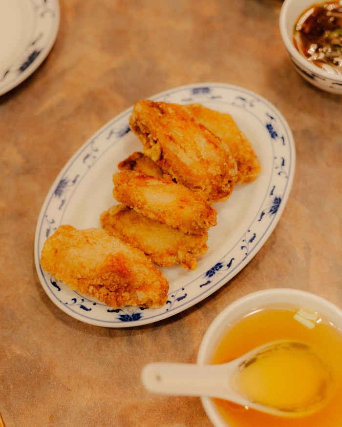 Deep-fried chicken wings sitting on an oval plate, with a bowl of lemon sauce beside it, at Max Noodle House